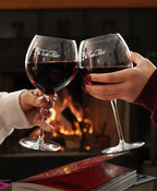 Two clear pinot noir wine glasses with the Plot Twist & Pinot logo in a white script font. Two glasses are filled halfway with wine.