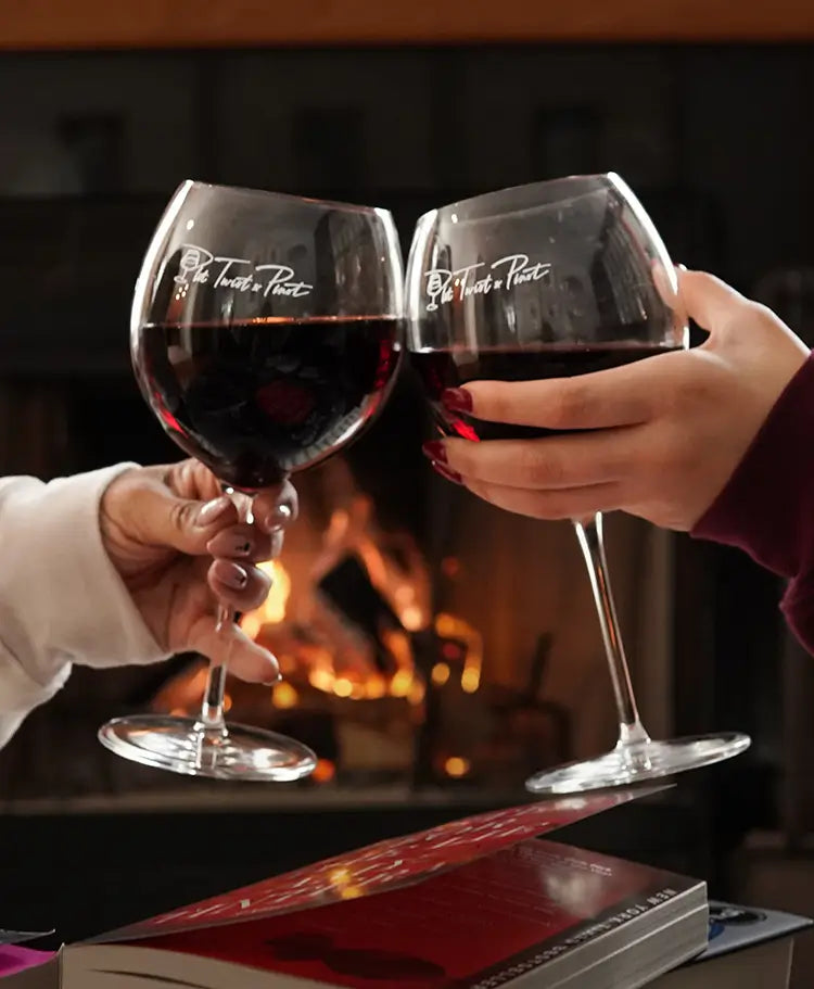 Two clear pinot noir wine glasses with the Plot Twist & Pinot logo in a white script font. Two glasses are filled halfway with wine.