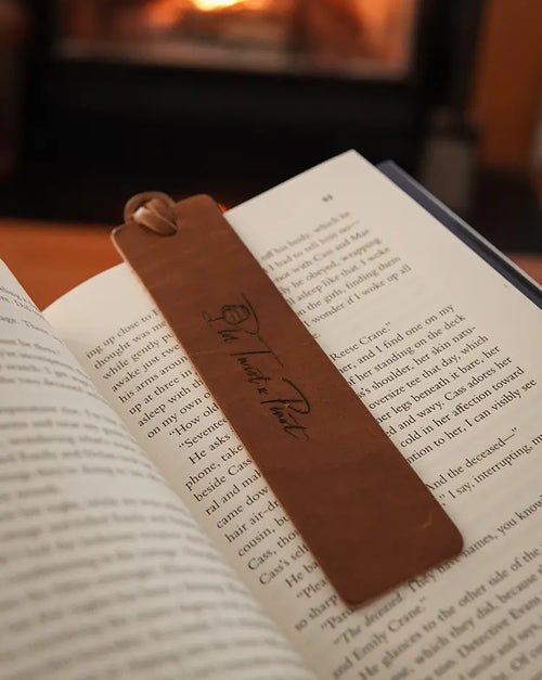 Open book with a leather suede bookmark with the Plot Twist and Pinot logo in script font and classic tassel.