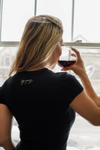 Back view of the black rib t-shirt, showing the small PTP logo in the upper back area, in same script font and cream coloring. 
