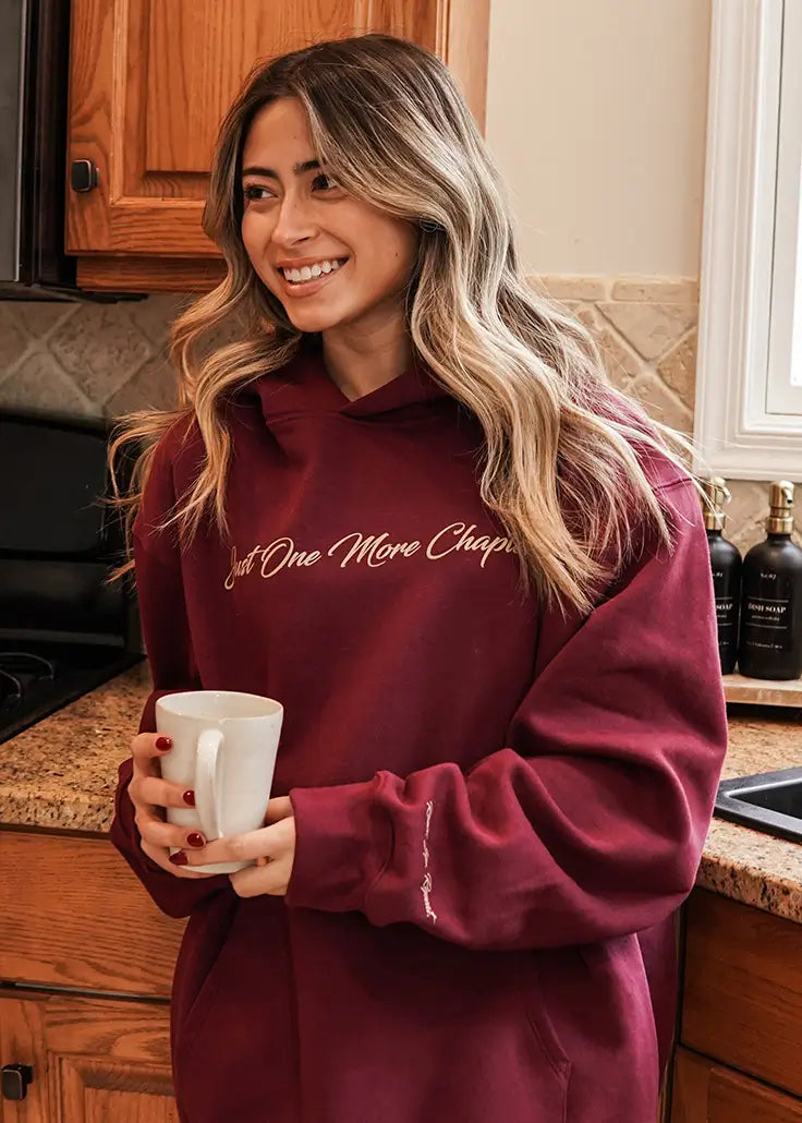 A woman wearing a maroon hoodie that reads "Just One More Chapter".