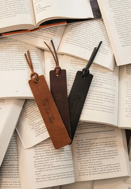 Three leather bookmarks in three colors, cognac, suede, and noir (black) laying on open books