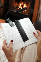 A woman reading a book in front of fireplace using the noir black bookmark.