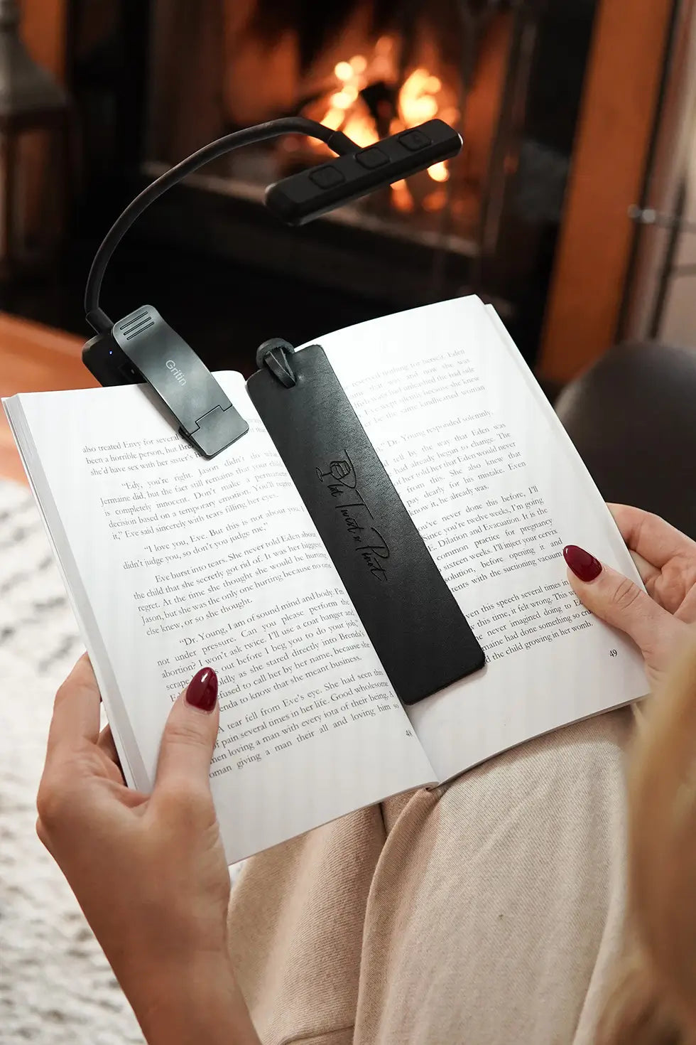 A woman reading a book in front of fireplace using the noir black bookmark.